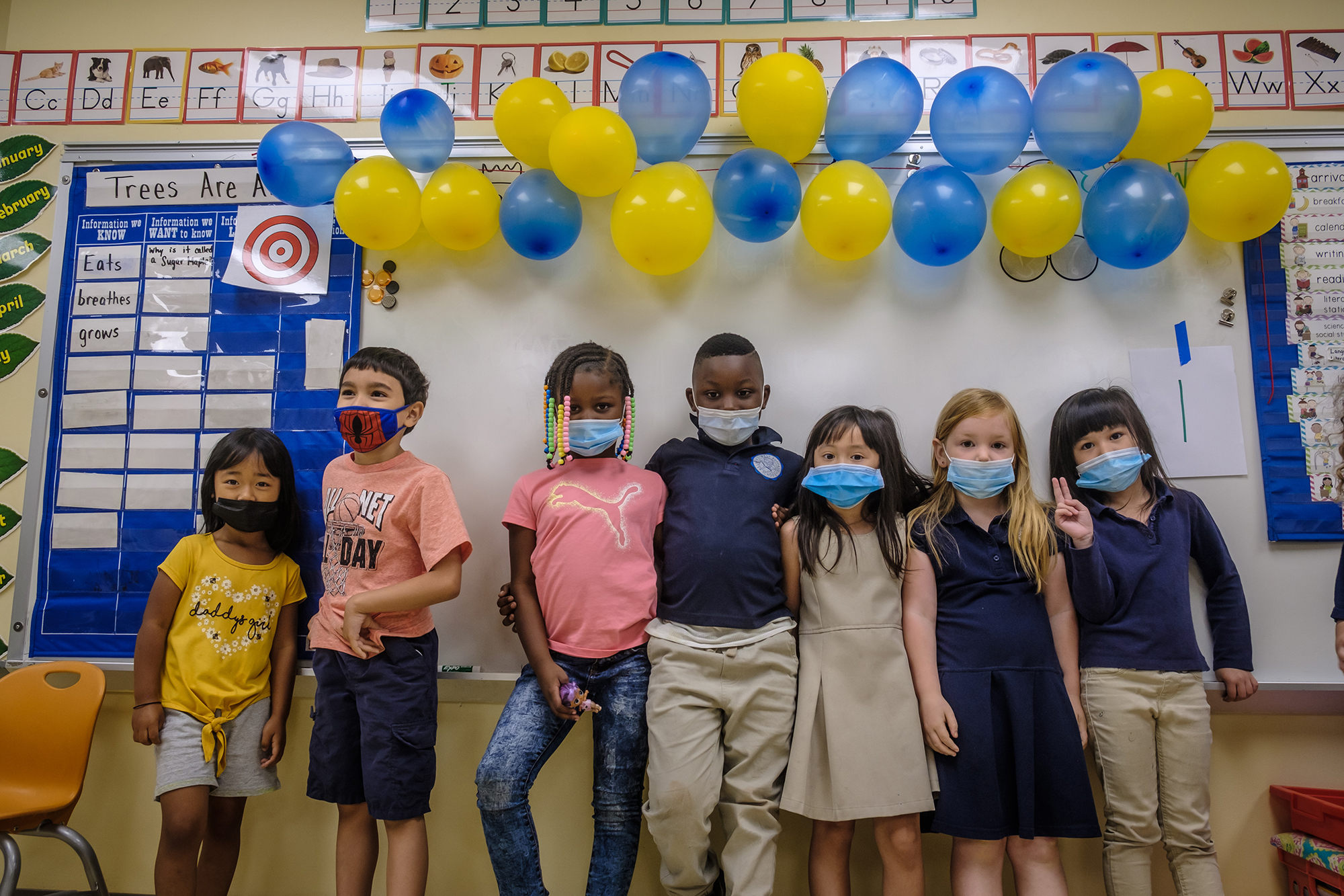 group of kids with masks on in a classroom standing in front of the white board