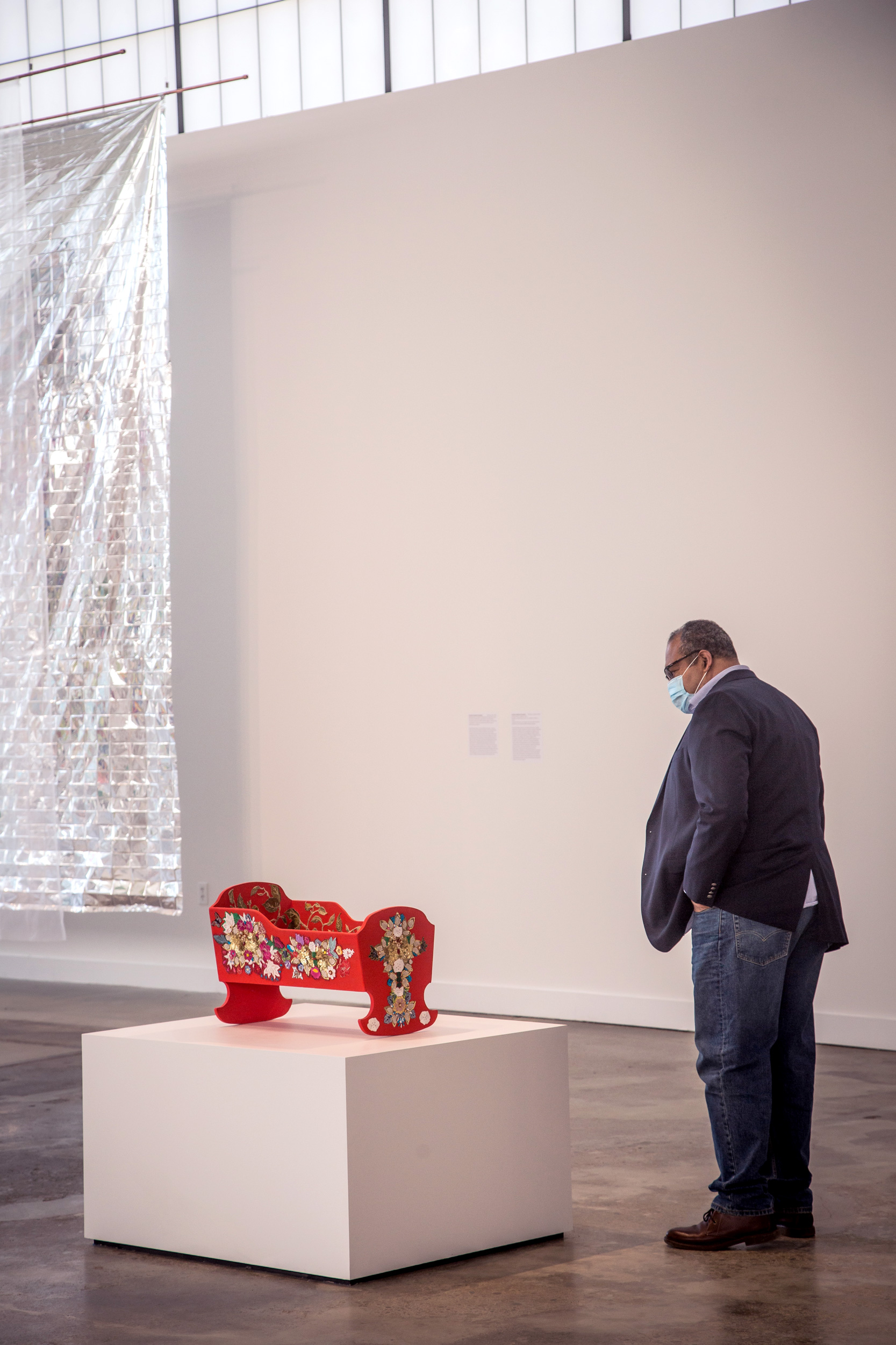 man with a mask on in a museum looking at beaded cradle art